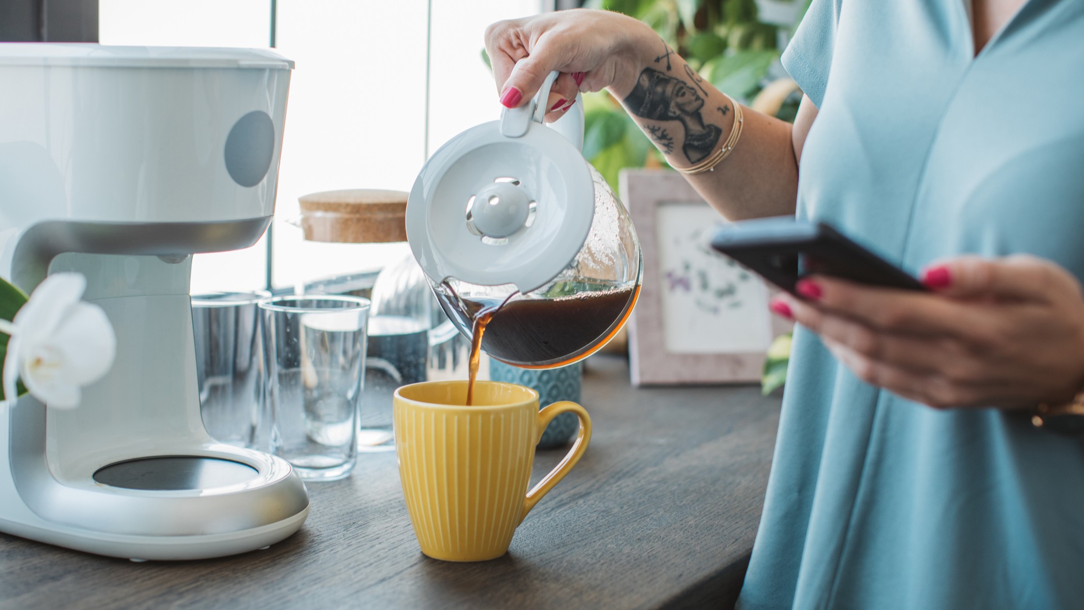 Person pouring filter coffee in kitchen while looking at smart phone